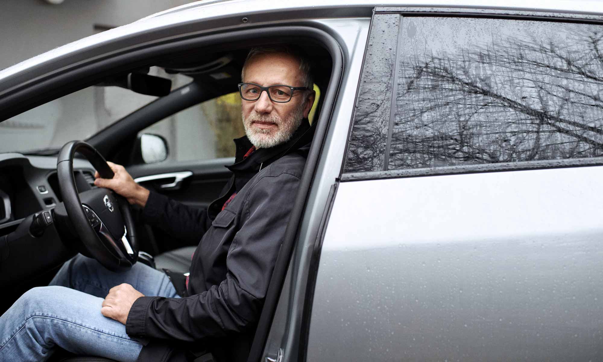 Äldre man med skägg och glasögon sitter i en bil en regnig dag